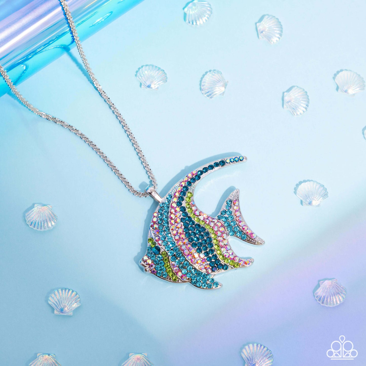 Silver angelfish charm necklace with green, blue, and iridescent rhinestones on a silver box chain against a blue seashell background